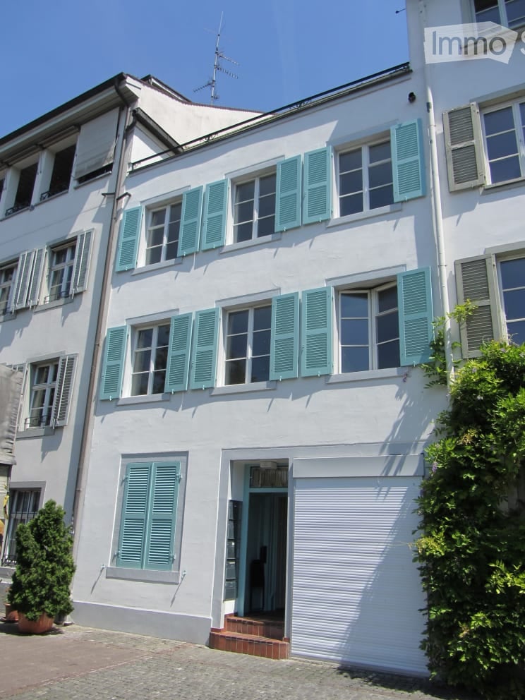 A three-story white house with blue shutters and a closed garage door. The entrance features a small staircase leading to a blue door.