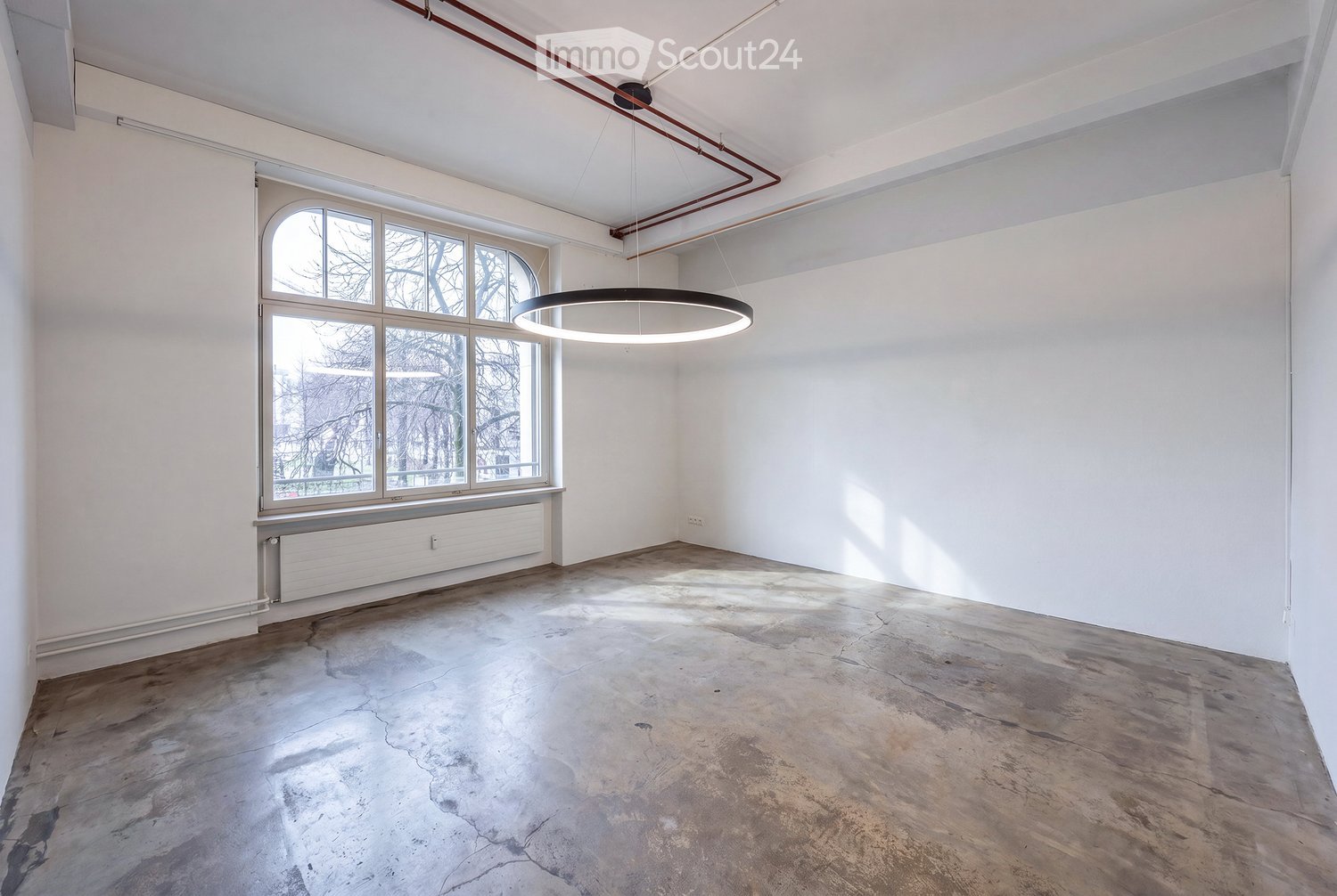Empty room with white walls, concrete floor, large window with multiple panes, and a modern pendant light fixture.