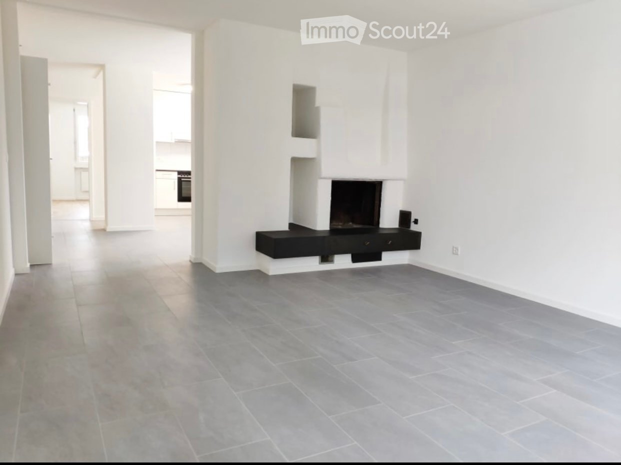 Empty living room with grey tiled floor, white walls, and a built-in fireplace with a black surround.