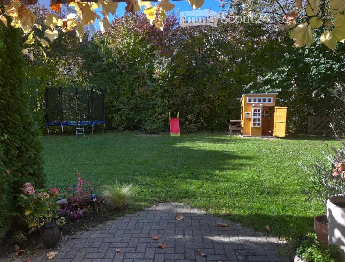 Well-maintained garden with a grassy lawn, a small yellow playhouse, a trampoline, a slide, and surrounding trees and shrubs.