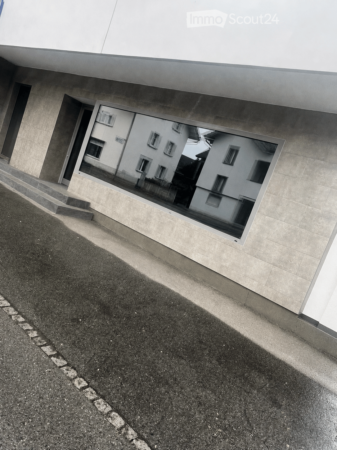 Modern building exterior with large reflective glass window, concrete steps leading up to entrance, and a raised ground floor.