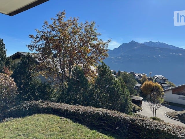 Balcony or terrace view overlooking a scenic valley with mountains, trees, and houses below.