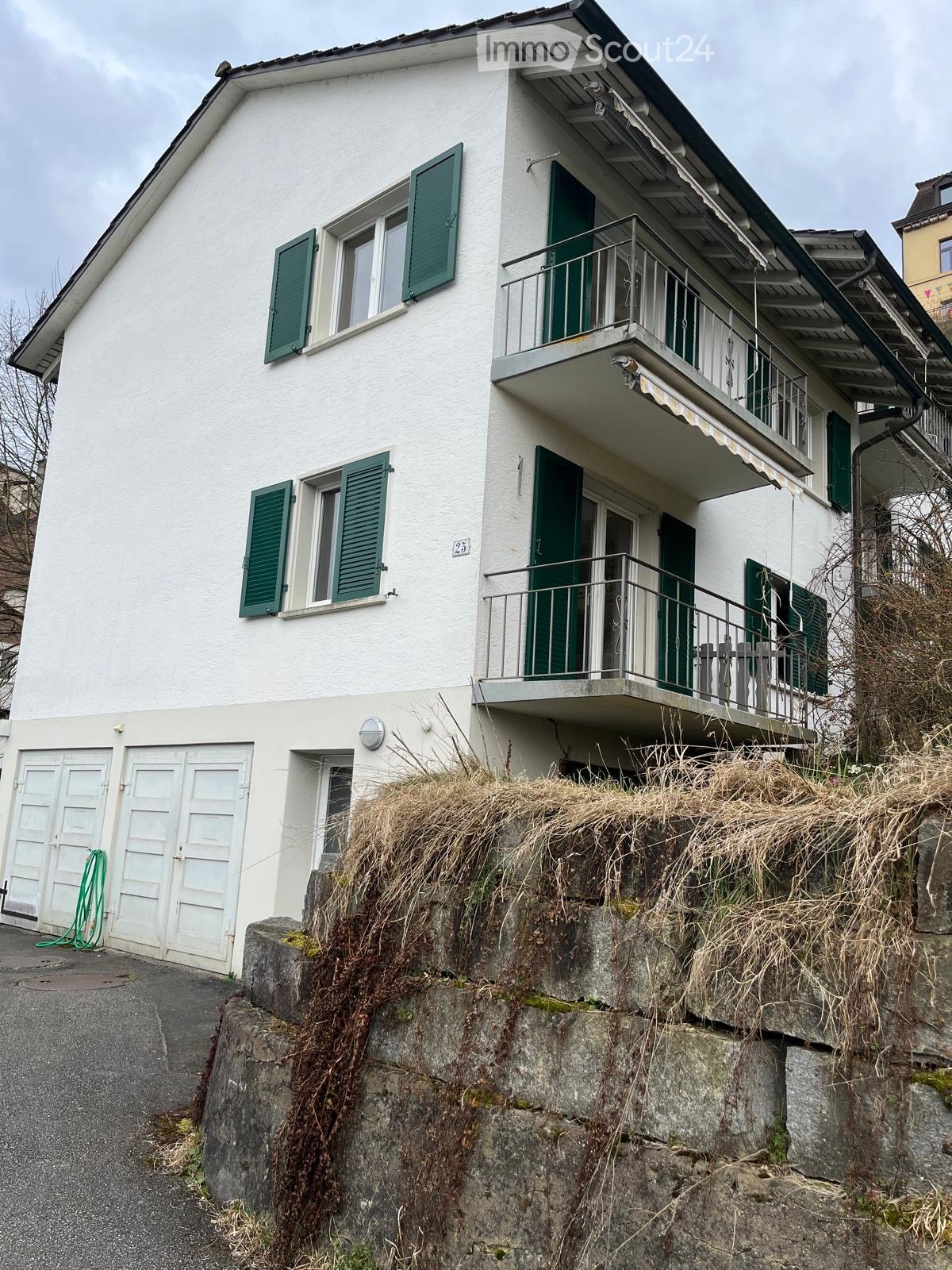 Two-story white house with green shutters, balcony, and garage.