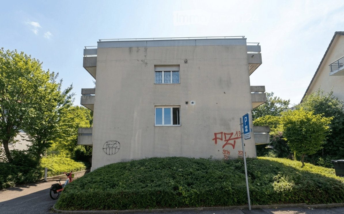 Four-story residential building with balconies, graffiti on the facade, and a parking sign nearby.