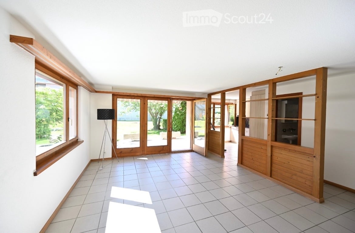 Empty room with tiled floor, white walls, large windows, and wooden sliding doors leading to an outdoor area.