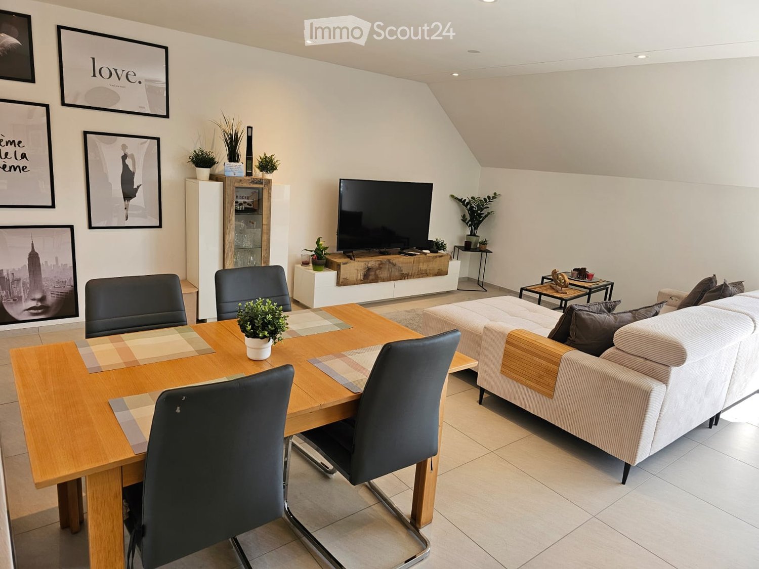 Modern living room with a white sofa, coffee table, dining table with chairs, television, and decorative plants.