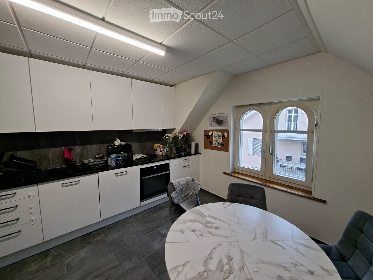 Modern kitchen with white cabinets, a marble dining table, and chairs, featuring a window with a view of the outside.
