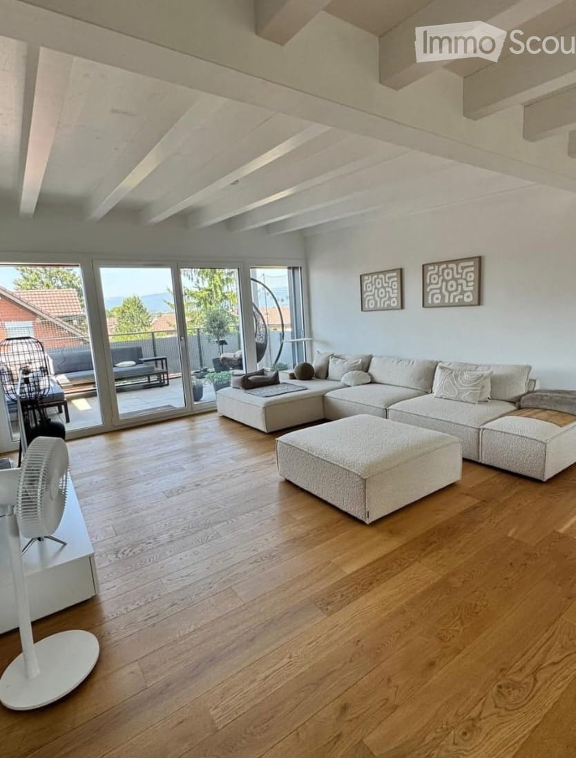 Modern living room with light-colored sectional sofa, ottoman, and a white fan. Large windows offer a scenic view of the outdoors.