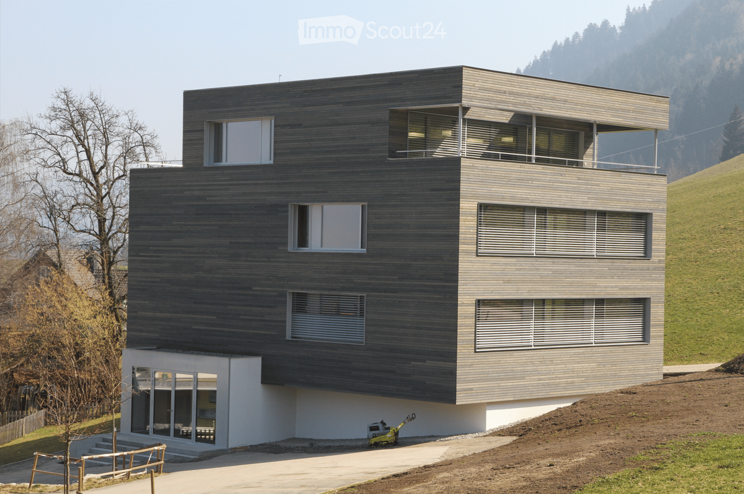 modern house, 3 levels, dark gray wooden facade, windows with white shutters, balconies