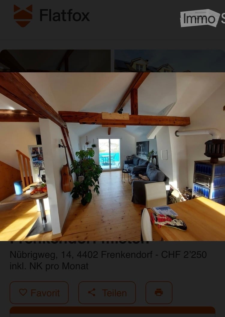 Bright, open-plan living and dining area with wooden floors, exposed wooden beams, large windows leading to a balcony, sofa, dining table, chairs, and a guitar leaning against the wall.