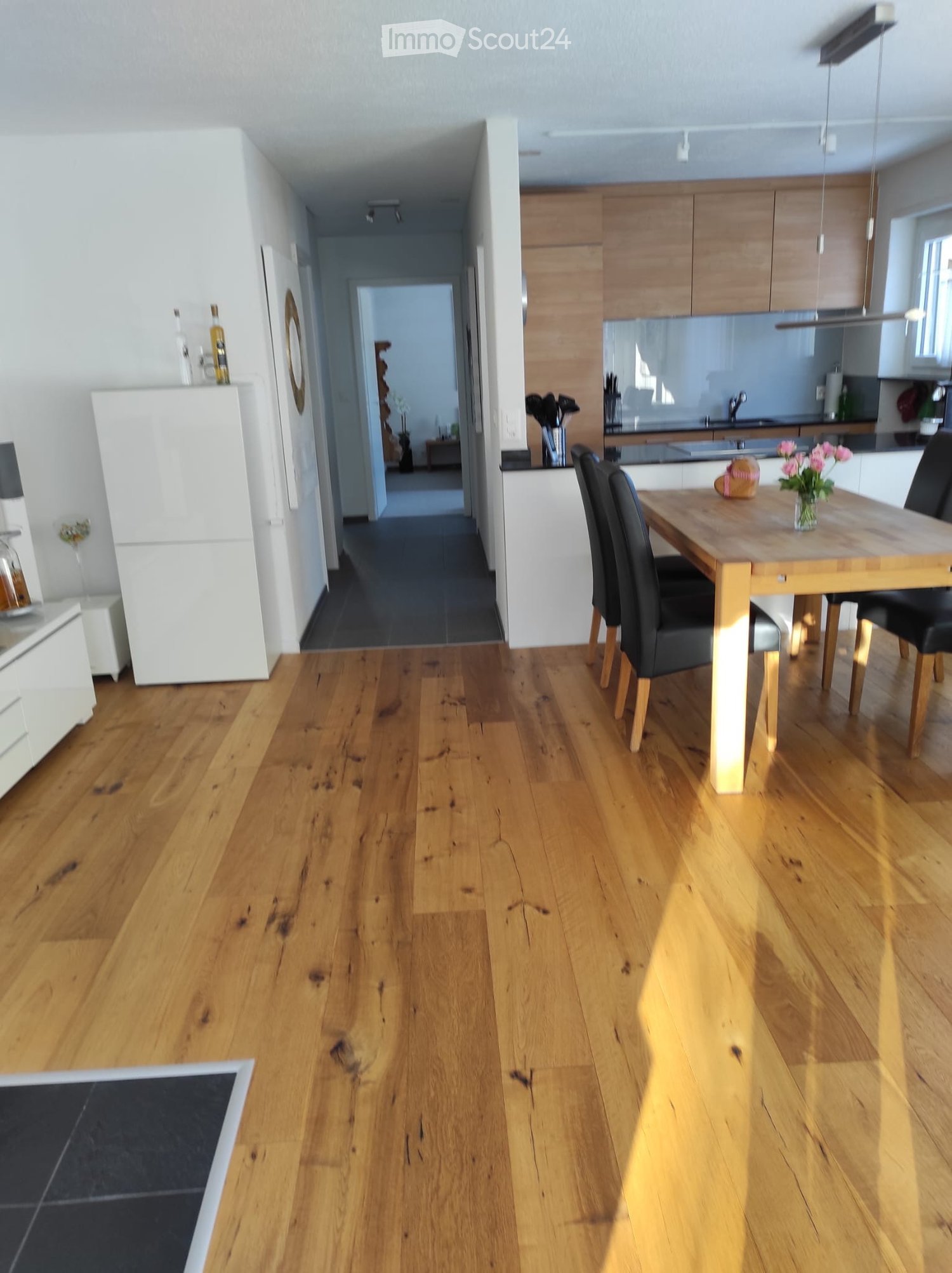 Open-plan kitchen and dining area with wooden flooring, modern cabinets, a dining table with chairs, and a refrigerator.