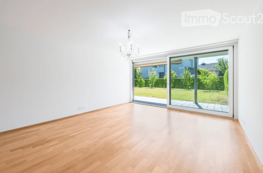 Empty room with light wooden flooring, white walls, and large sliding glass doors leading to a garden area.