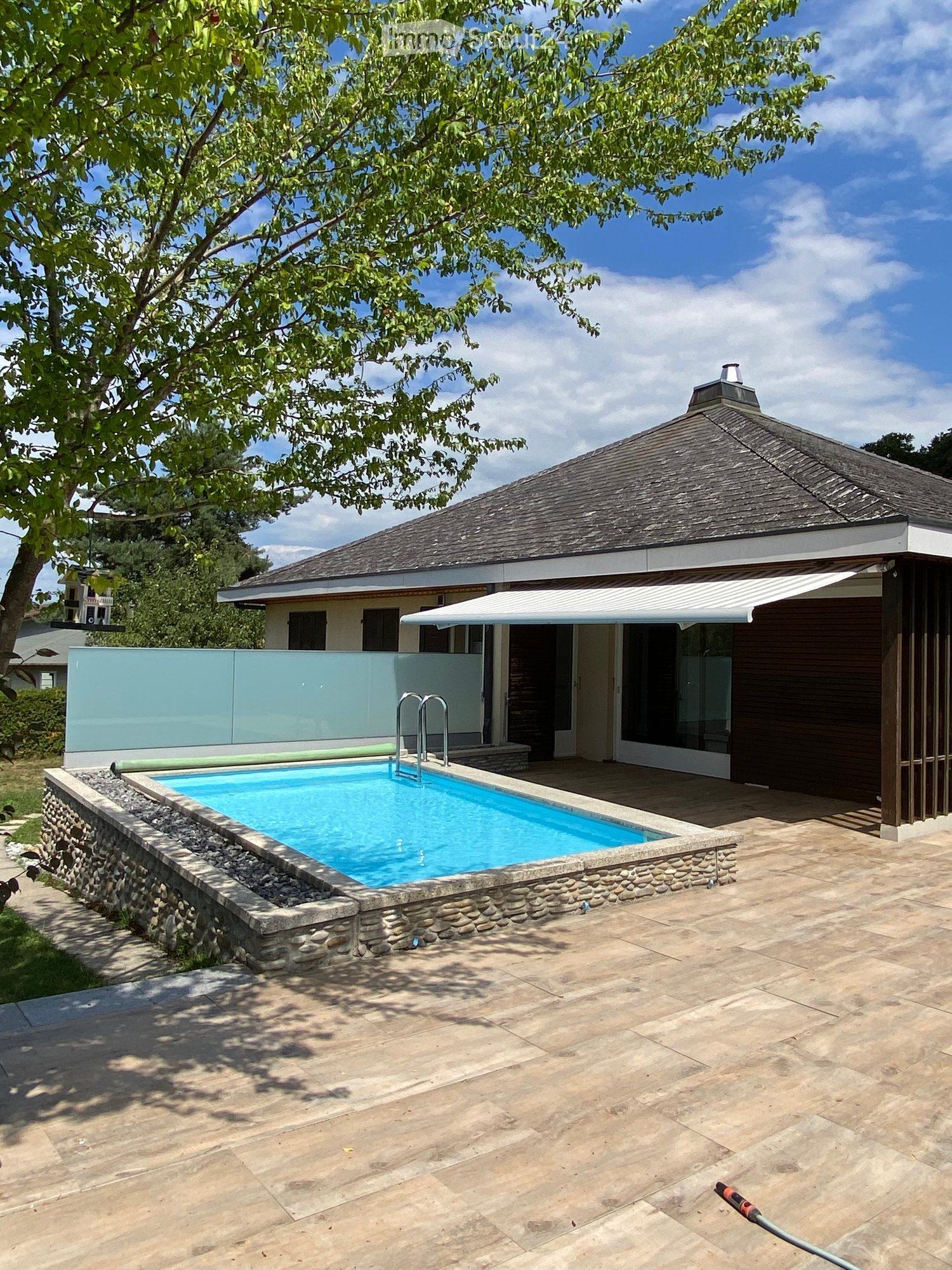 Two-story house with a swimming pool, surrounded by trees and a patio area with a glass balcony or terrace.