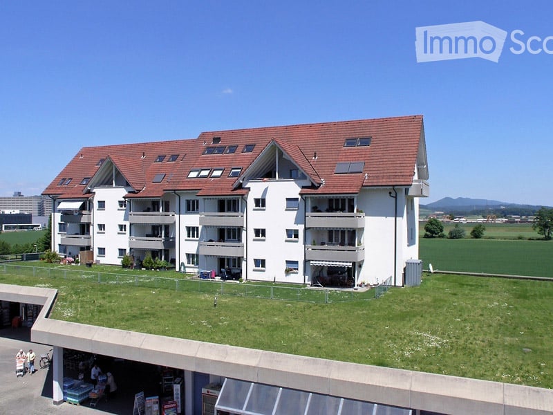Multi-story residential building with white exterior, red-tiled roof, multiple balconies, and a green rooftop area.