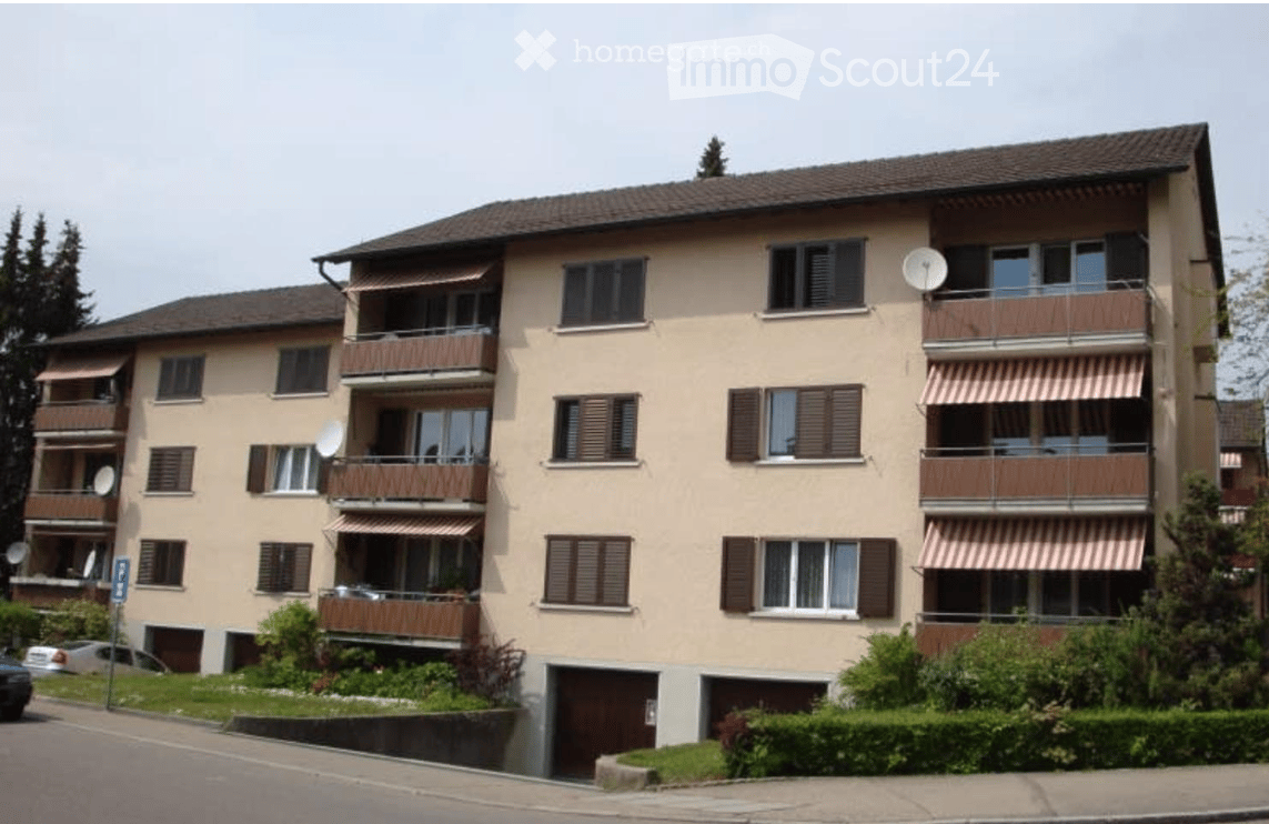 Four-story residential building with balconies, satellite dishes, and a garage entrance.