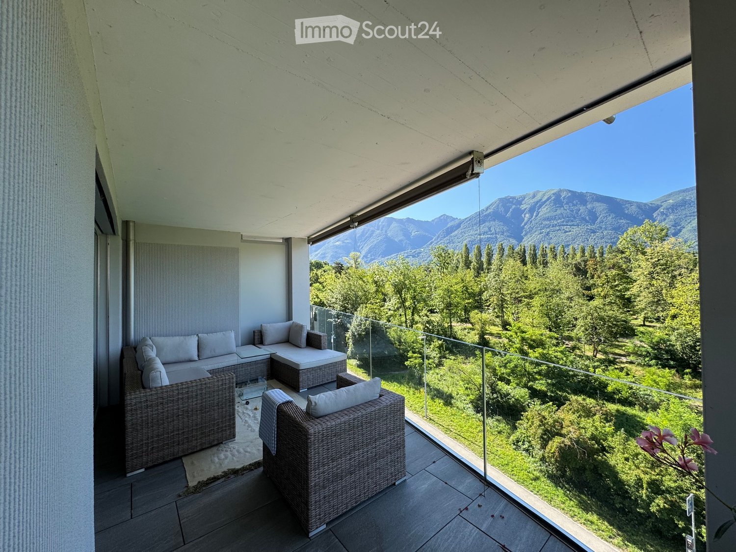 Balcony with modern wicker furniture, including a sofa, chairs, and a small table, overlooking a scenic mountain and forest view.