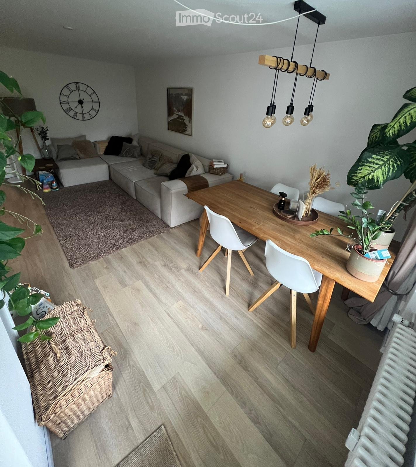 Modern living and dining area with a sectional sofa, coffee table, dining table with chairs, pendant lights, and decorative plants.