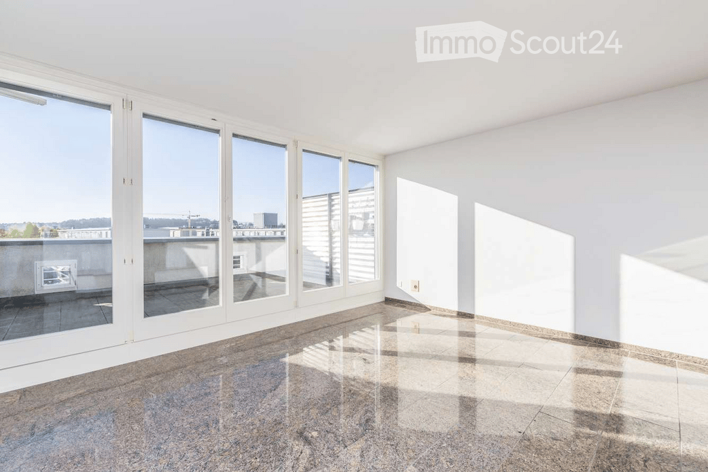 Empty room with large windows and a view of a balcony area. The floor is tiled, and the walls are white.
