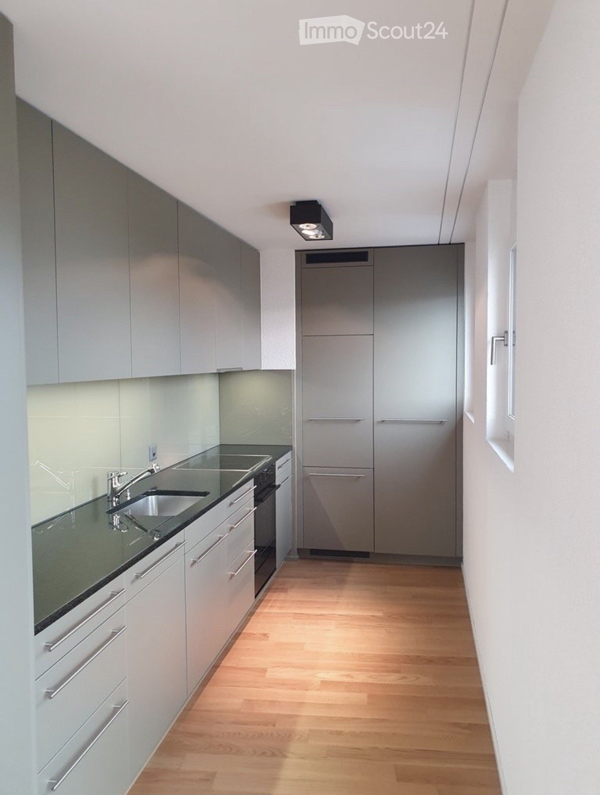 Modern kitchen with light grey cabinets, stainless steel appliances, and a wooden floor.