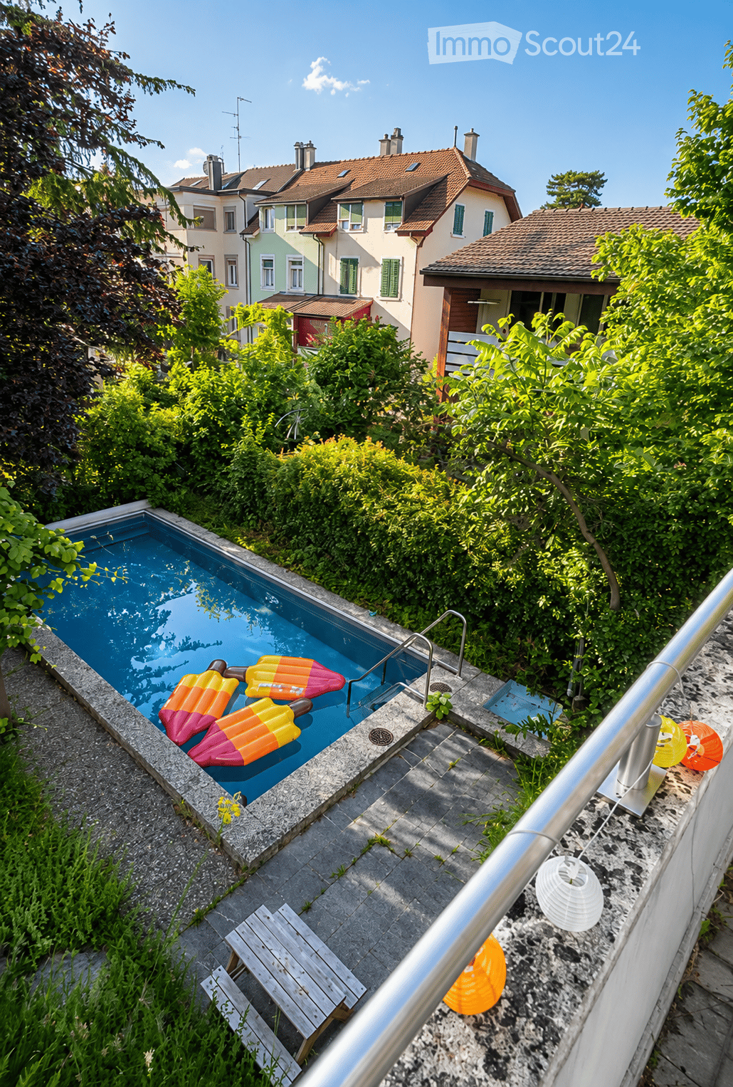 A small swimming pool surrounded by greenery, with inflatable ice cream-shaped floats in the water, a wooden bench, and decorative lanterns nearby.