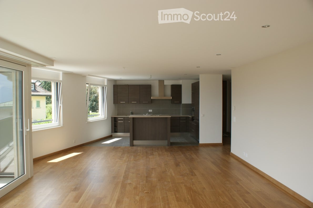Open-plan living and kitchen area with wooden flooring, modern kitchen cabinets, and large windows with balcony access.