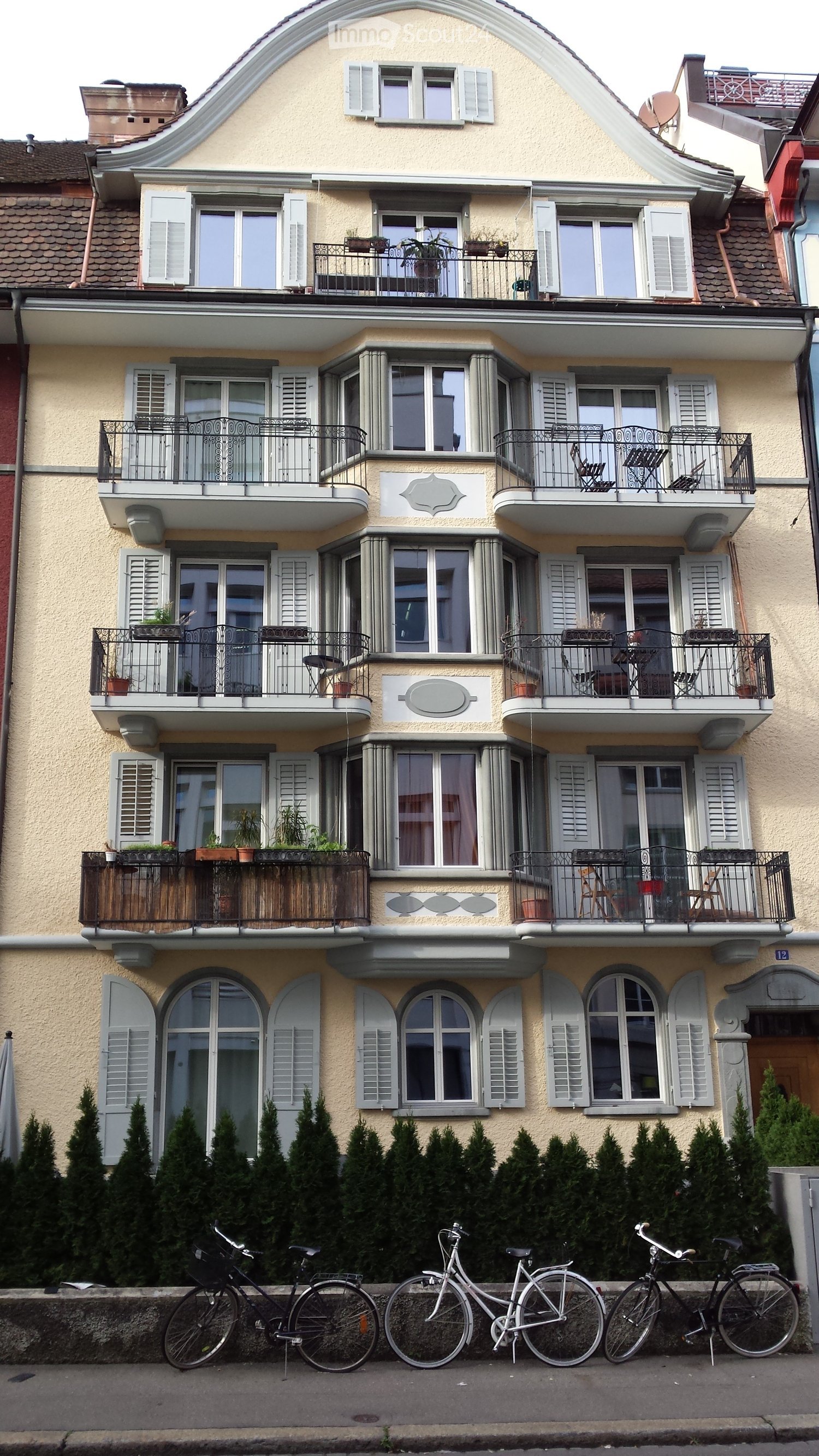 4 story building, beige paint, white shutters, balconies, windows, metal railings, potted plants
