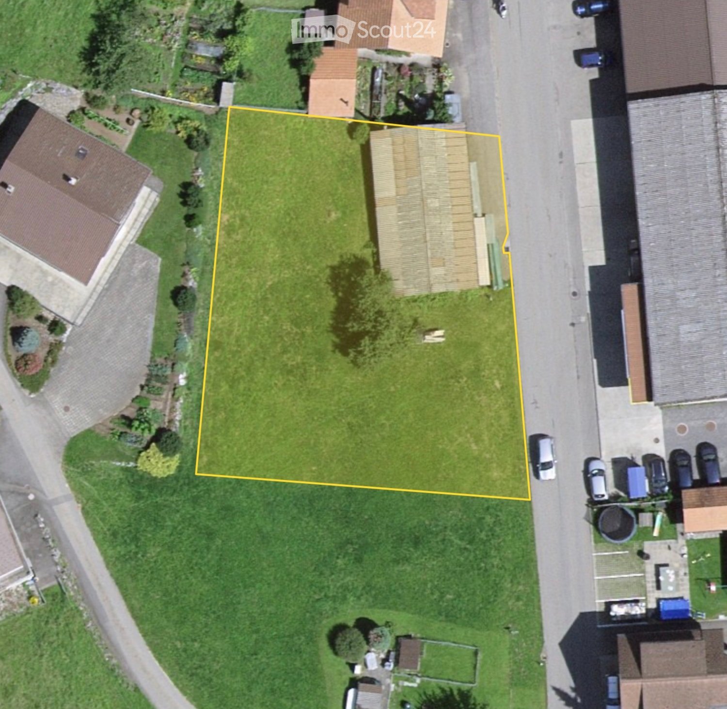 Aerial view of a residential area with a highlighted plot of land surrounded by neighboring houses, trees, and parked cars.