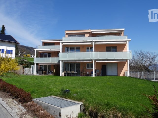 Two-story house with balconies, light pink facade, and a well-maintained green lawn in front.