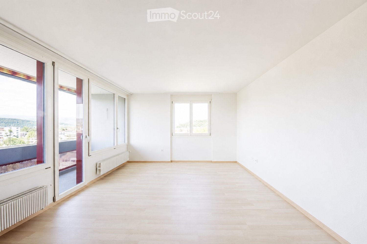 Empty room with light wooden flooring, white walls, large windows, and a balcony view.