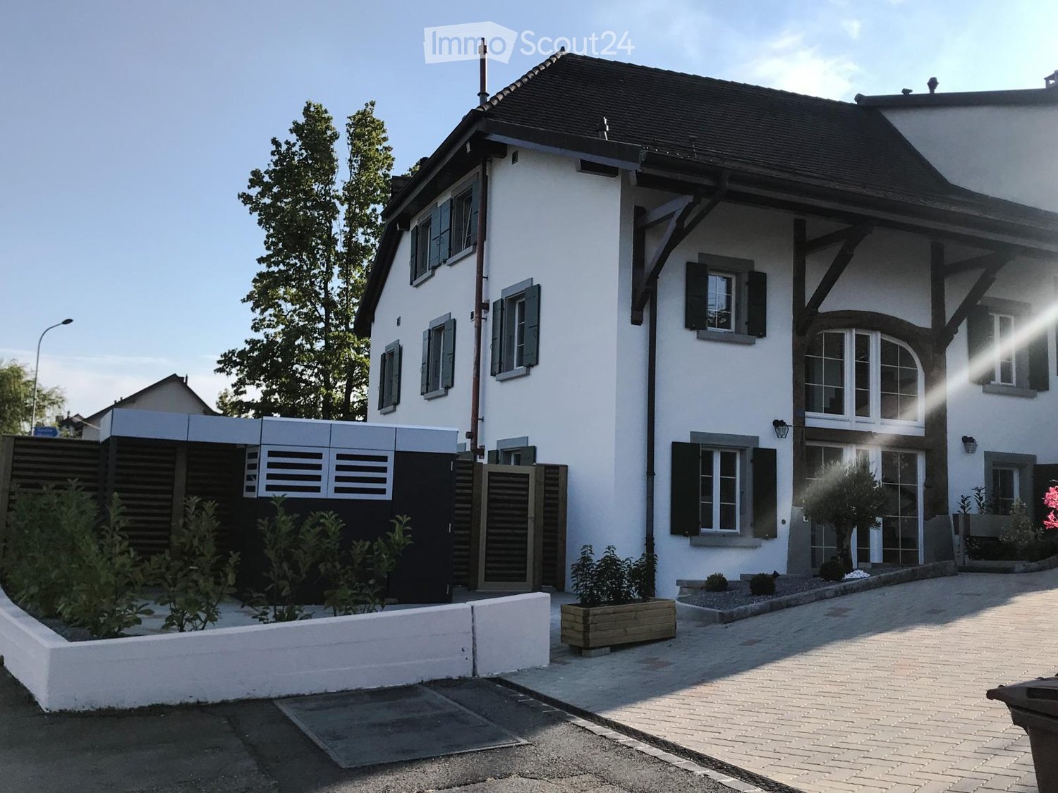 Two-story white house with dark roof, multiple windows with shutters, garage, and landscaped garden area.