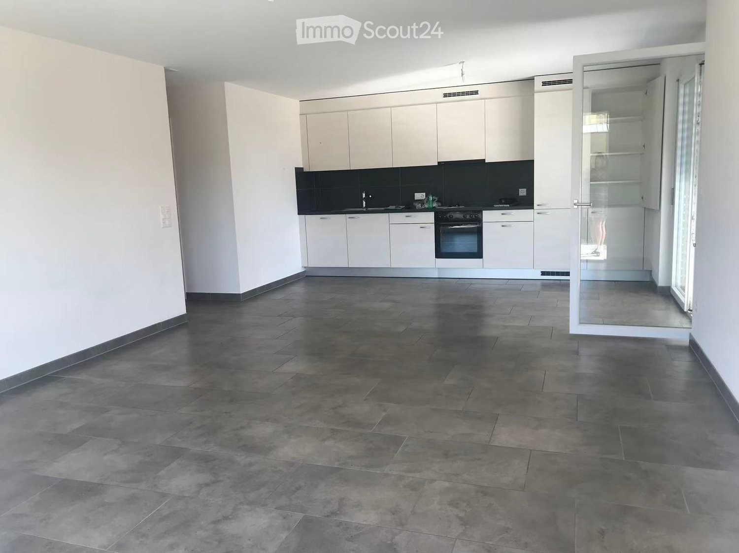 Empty kitchen with white cabinets, dark countertops, and a tiled floor. No furniture or appliances are present.