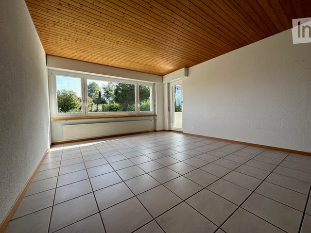 Empty room with tiled floor, wooden ceiling, large windows, radiator, and white walls.