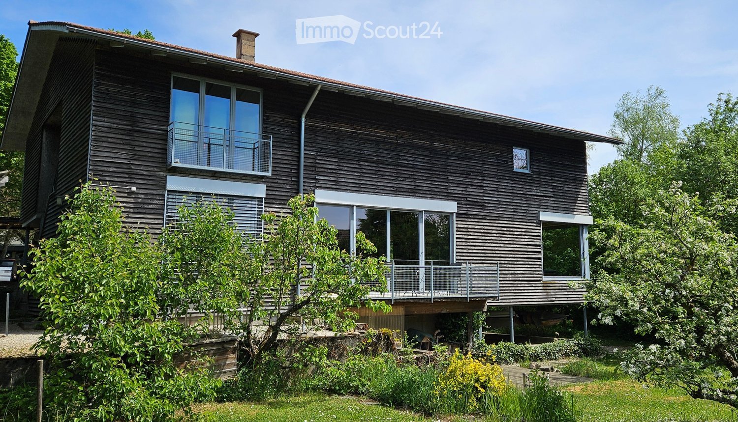 House. Modern two-story wooden house with large windows, balconies, and a well-maintained garden.