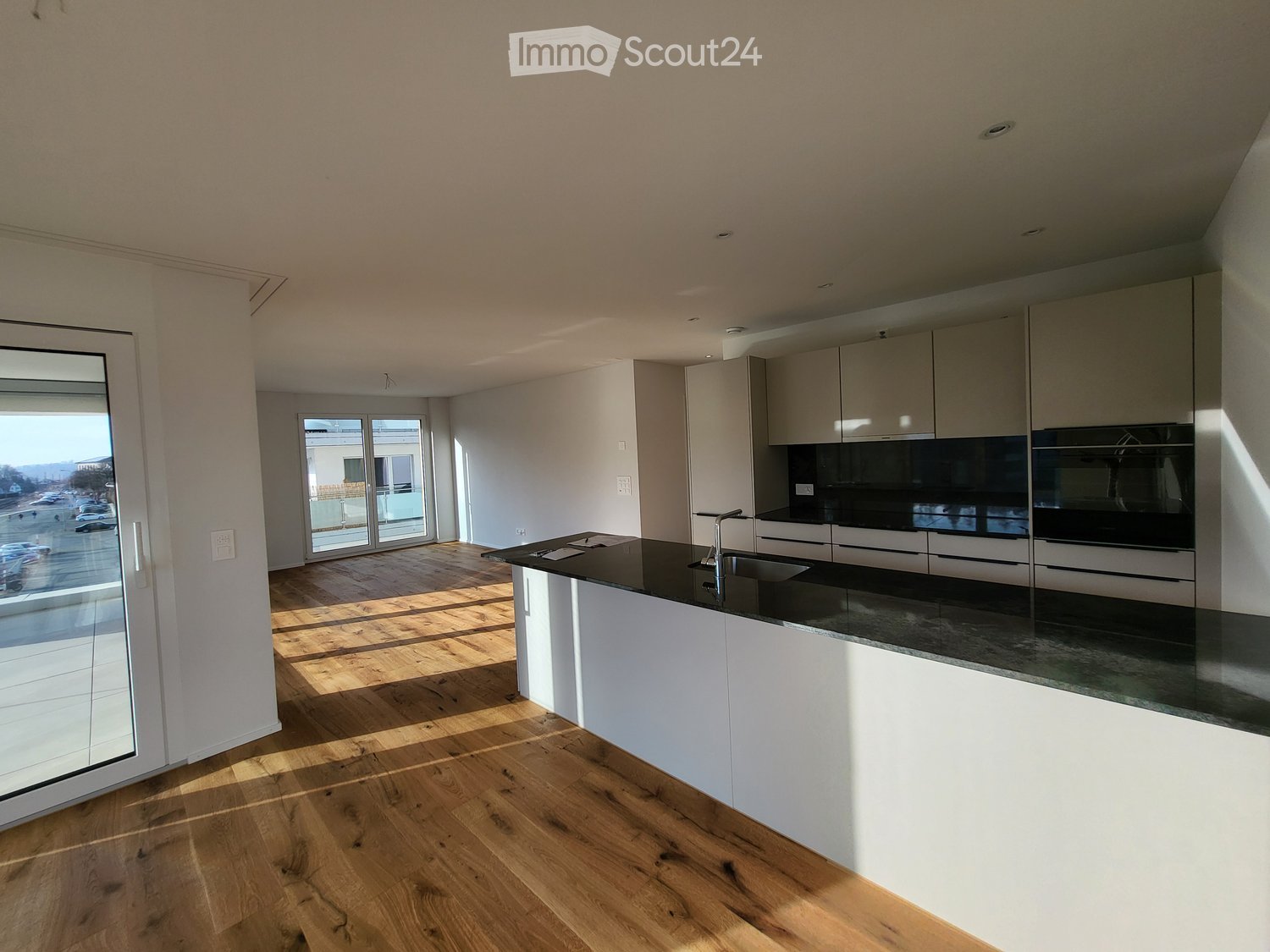 Modern kitchen with white cabinets, black countertops, wooden flooring, and large windows letting in natural light.