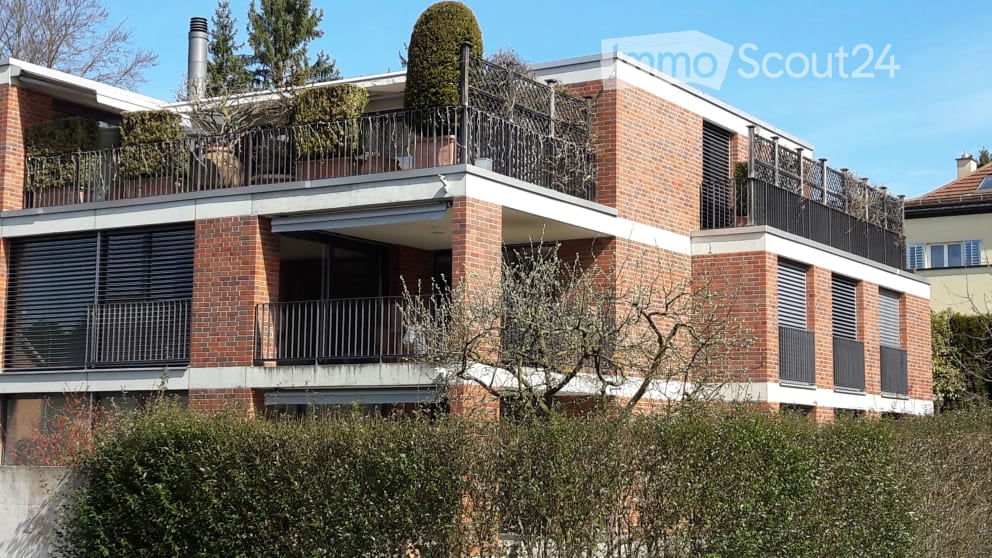 Modern brick apartment building with multiple balconies and greenery on the roof.