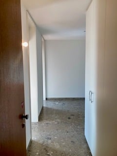 Empty hallway with white walls, concrete floor, and a closed wooden door on the left side.