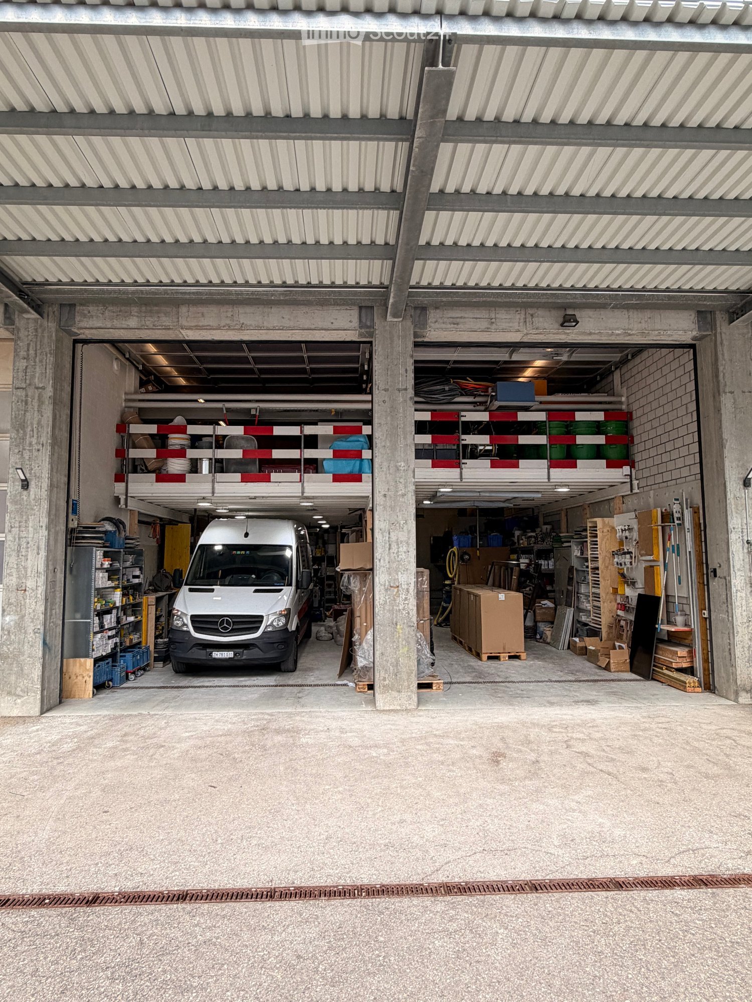 Large, open garage with concrete floors and walls, featuring a parked van, shelves with storage items, and various tools and equipment.