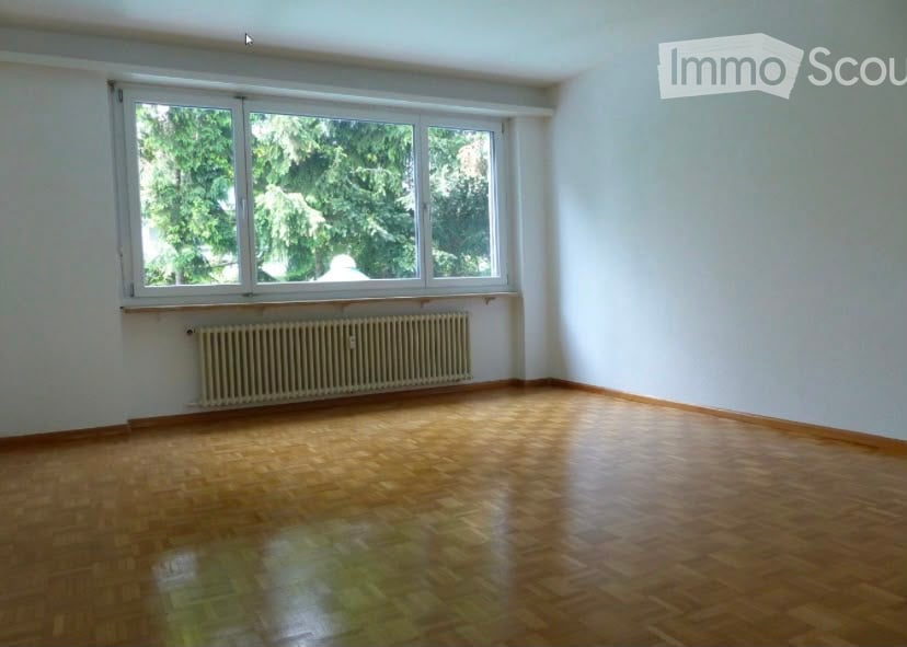 Empty room with wooden flooring, large window, radiator, and white walls.