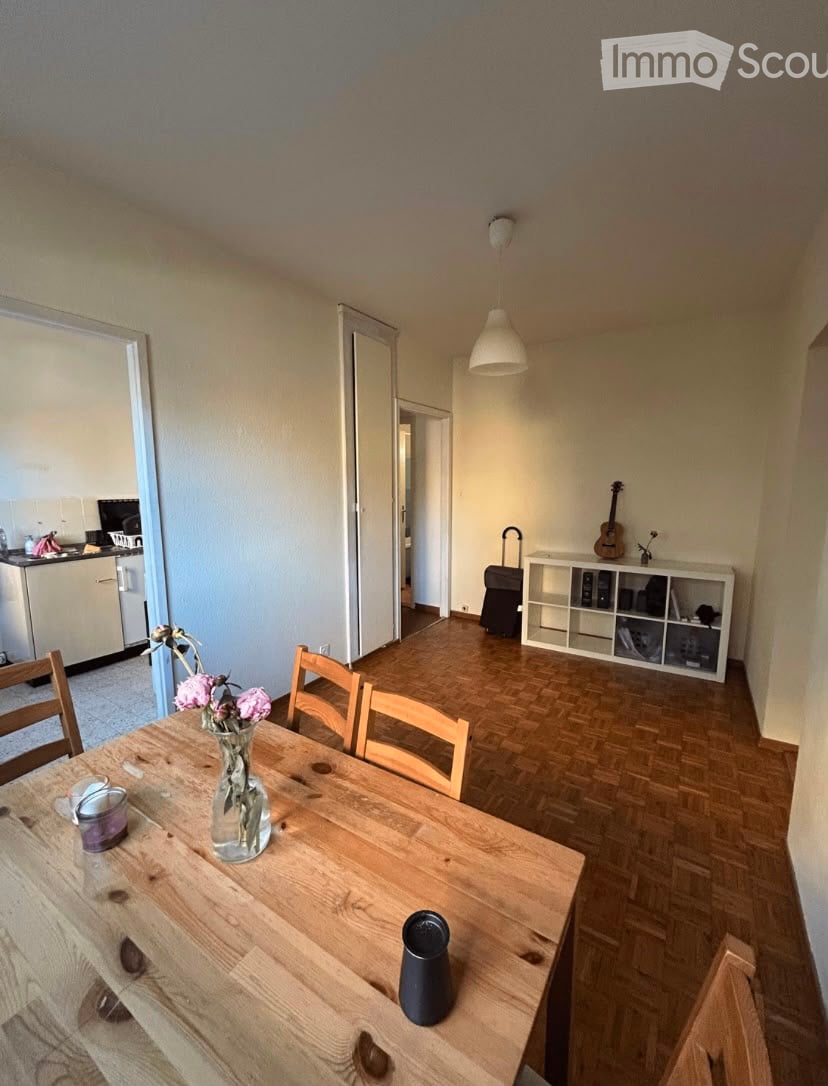 A well-lit dining area with a wooden table, chairs, a vase with flowers, and a guitar on a shelf. The room features wooden flooring and a modern aesthetic.