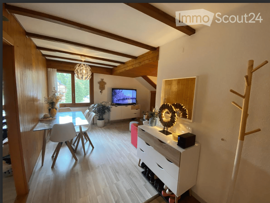 Bright, modern dining area with a glass dining table, white chairs, a large window, a TV, and a shoe cabinet. The room features wooden beams on the ceiling and a sleek, contemporary design.