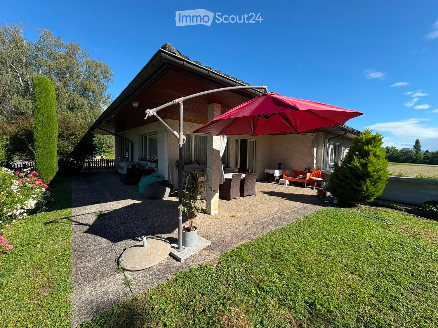 Outdoor patio area with a large umbrella, dining table, chairs, and a small garden with grass and flowers.