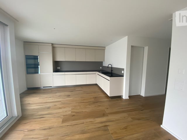 Empty kitchen with light-colored cabinets, dark countertops, and wooden flooring. No furniture or appliances are present.