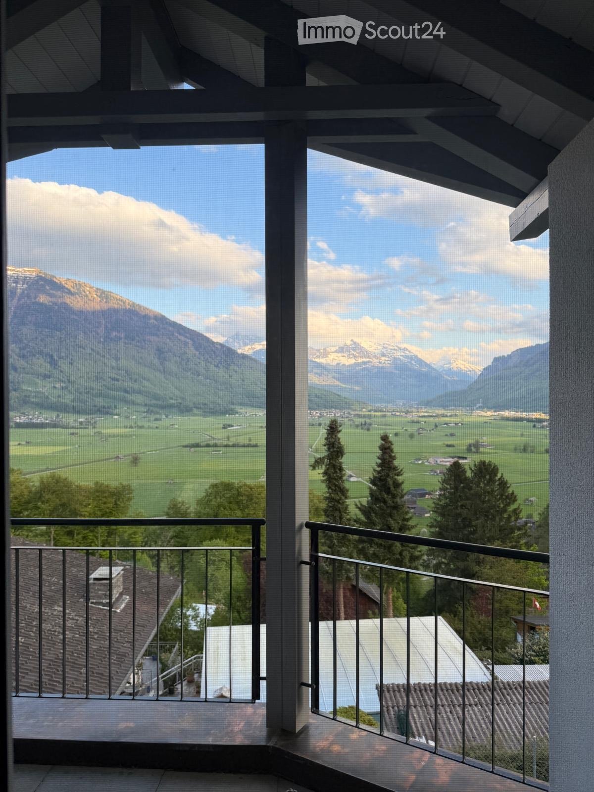 Balcony with metal railing, offering panoramic views of mountains, fields, and a village below.