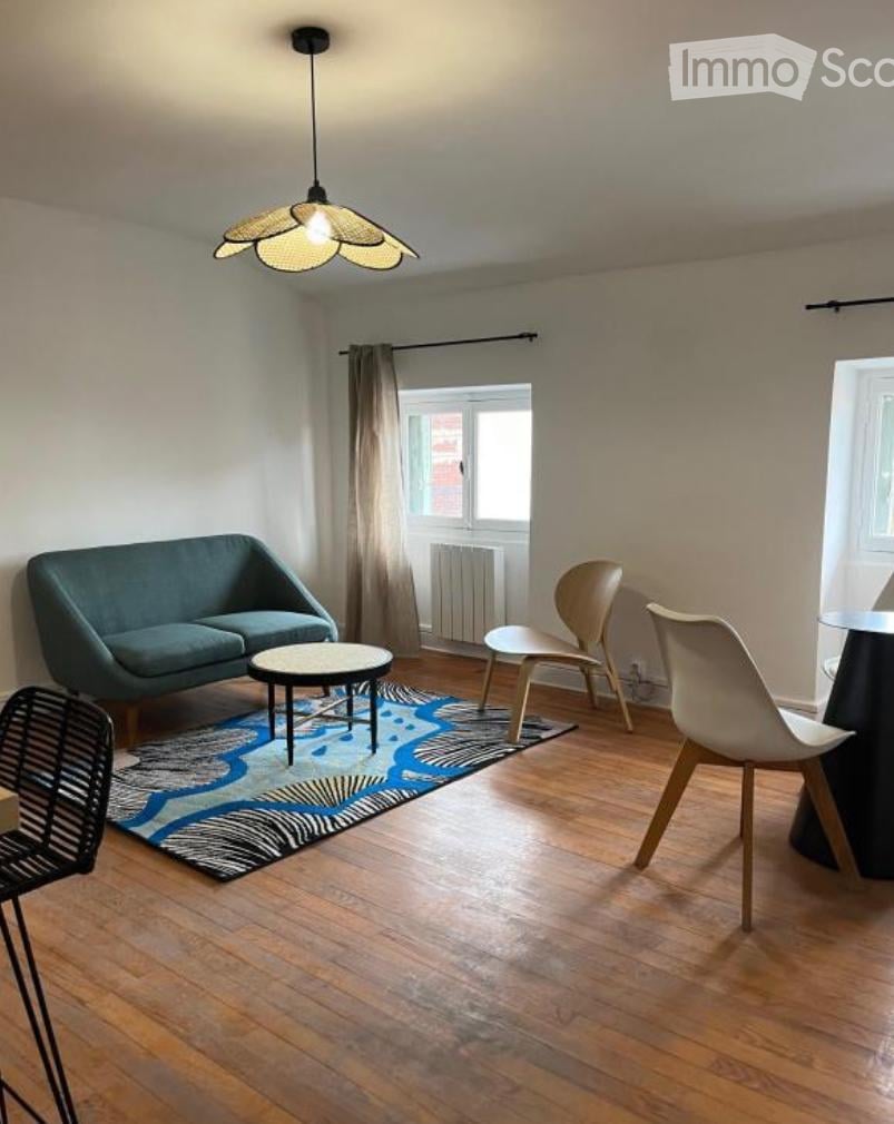 Modern living room with wooden flooring, a blue sofa, a coffee table, and several chairs arranged around a patterned rug.