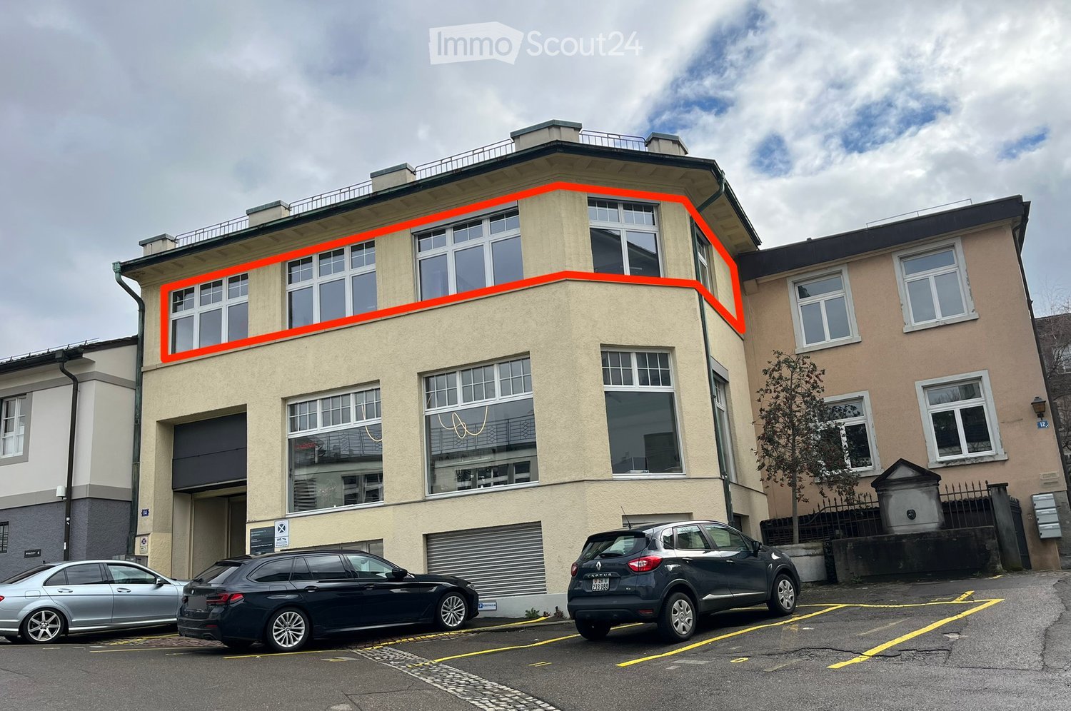 3 story building, beige exterior, glass windows, highlighted portion with orange line, garage on the ground floor, 3 cars parked in front