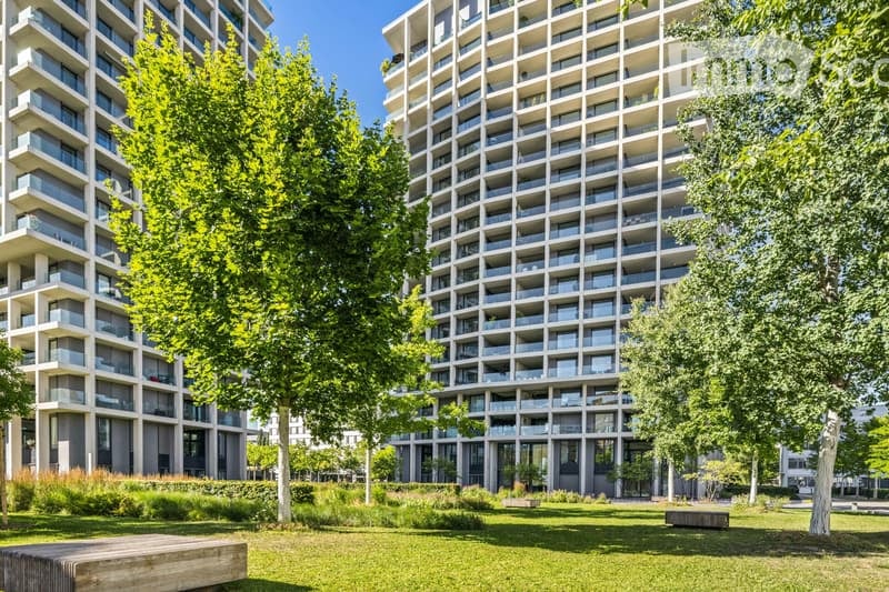Modern high-rise residential building with multiple balconies and large windows, surrounded by green spaces and trees.