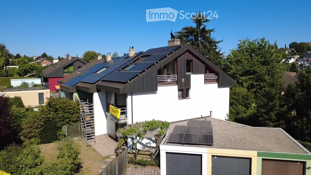 Two-story house with solar panels on the roof, white and dark brown exterior, garage, and surrounding greenery.