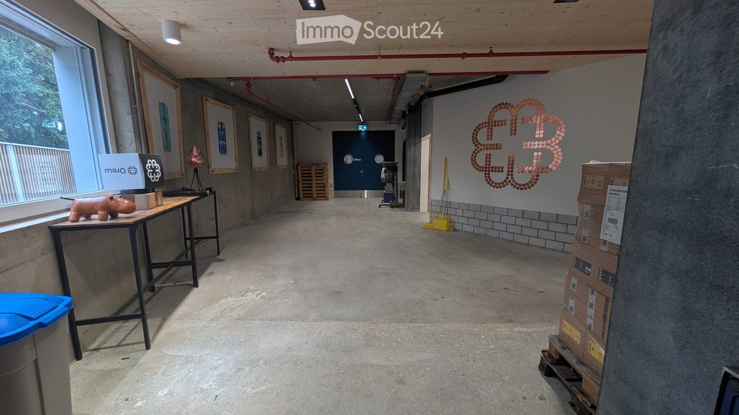 Empty hallway with concrete floor, exposed wooden ceiling, large windows, artwork, and a small table with a figurine.