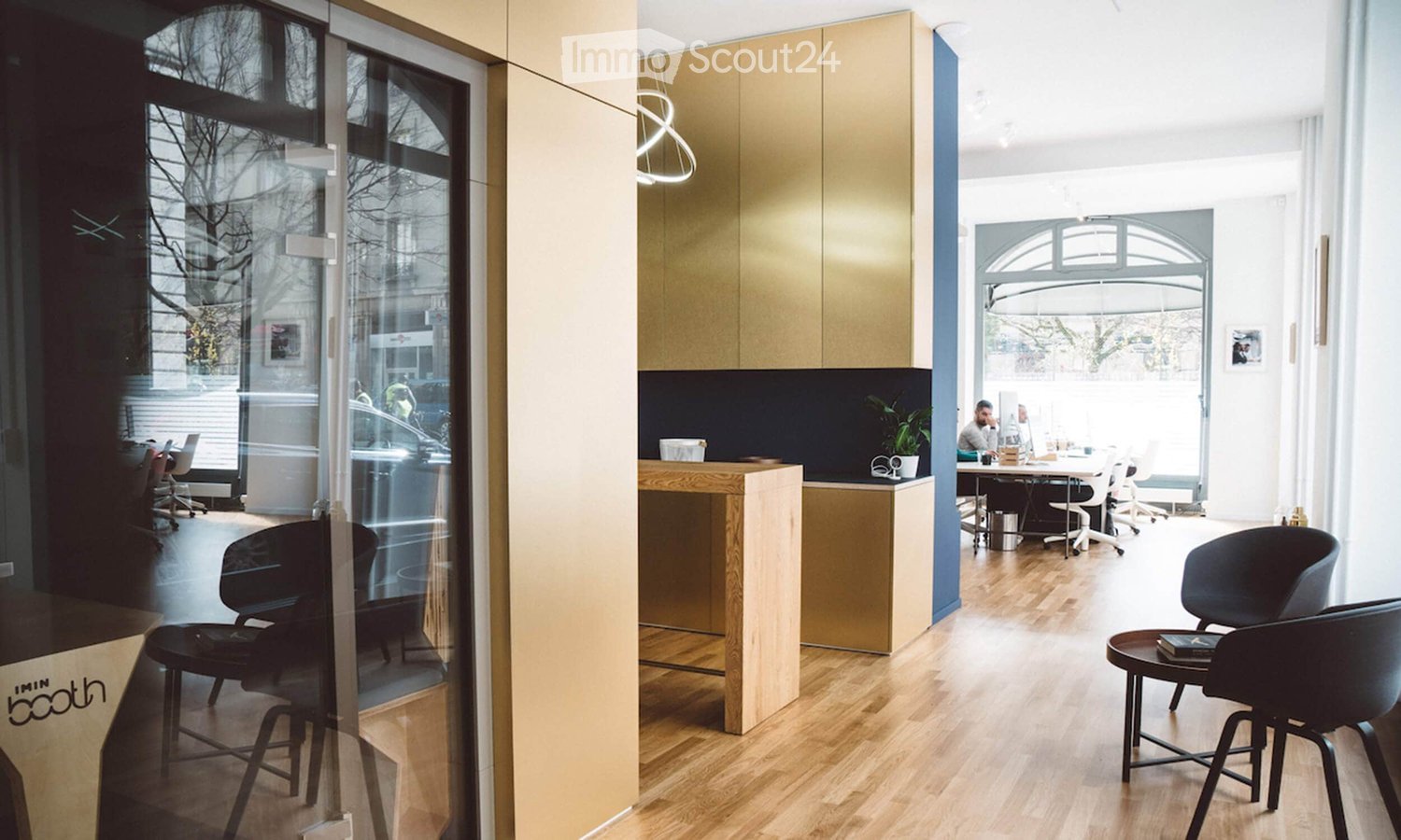 Modern office space with light wood flooring, glass walls, and contemporary furniture including chairs, tables, and a cabinet.