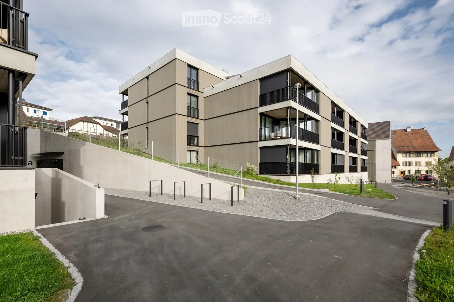Modern apartment building with balconies, concrete driveway, landscaped area
